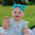 Baby girl smiling in blue bow at Riverside Park in La Crosse