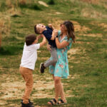 Mother holding her two sons on a hiking trail at sunset