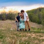Mother holding her two sons on a hiking trail at sunset