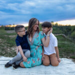Mother holding her two sons on a hiking trail at sunset