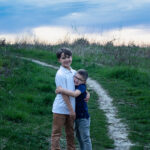 Mother holding her two sons on a hiking trail at sunset