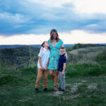 Mother holding her two sons on a hiking trail at sunset