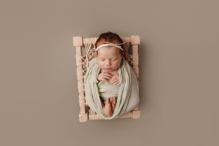Newborn baby girl wrapped in luxury fabric on cream prop bed, photographed by Onalaska newborn photographer Jodee Wallin